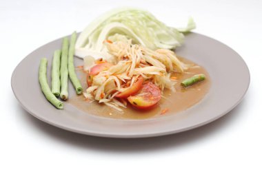 Tabakta Tayland papayası salatası, kakalı papaya salatası, limon, biber, beyaz bir masada gri bir tabakta kırmızı domates..