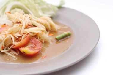 Tabakta Tayland papayası salatası, kakalı papaya salatası, limon, biber, beyaz bir masada gri bir tabakta kırmızı domates..