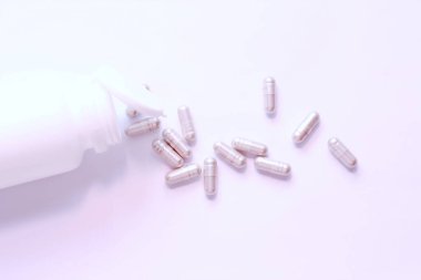 Gri hap kapsülleri ve ilaç şişeleri beyaz bir masaya yerleştirildi..