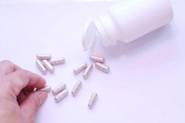 Gri hap kapsülleri ve ilaç şişeleri beyaz bir masaya bir adamın eliyle yerleştirilmiş..