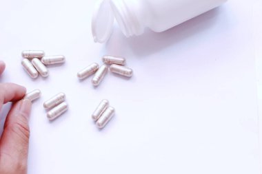 Gri hap kapsülleri ve ilaç şişeleri beyaz bir masaya bir adamın eliyle yerleştirilmiş..