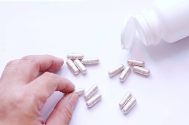 Gri hap kapsülleri ve ilaç şişeleri beyaz bir masaya bir adamın eliyle yerleştirilmiş..