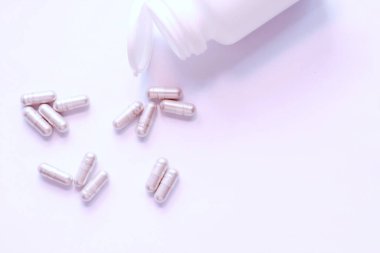 Gri hap kapsülleri ve ilaç şişeleri beyaz bir masaya yerleştirildi..