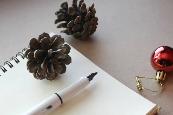 空白のノート 乾燥した松のコーン クリスマスボールと小さなギフトボックス 再生紙の上に置く — ストック写真