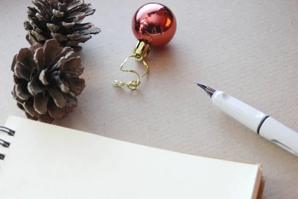 空白のノート 乾燥した松のコーン クリスマスボールと小さなギフトボックス 再生紙の上に置く — ストック写真