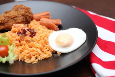 Amerikan pilavı sosis, salatalık, doğranmış sebze ile servis edilir. Beyaz bir masada, baharatlı bir tabakta..