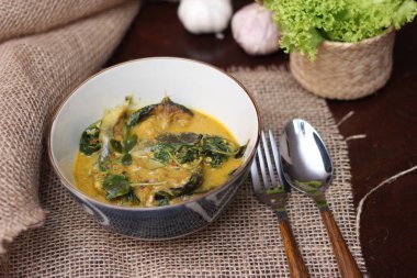 Tabak şeklinde bir kapta servis edilen kimyon yapraklı yayın balığı Curry. Kahverengi ahşap masada.