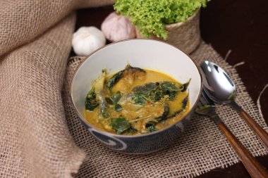 Tabak şeklinde bir kapta servis edilen kimyon yapraklı yayın balığı Curry. Kahverengi ahşap masada.