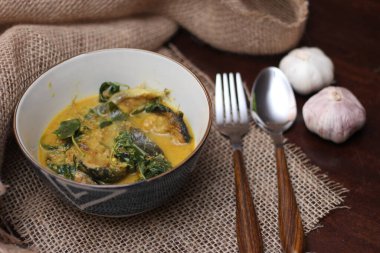 Tabak şeklinde bir kapta servis edilen kimyon yapraklı yayın balığı Curry. Kahverengi ahşap masada.