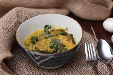 Tabak şeklinde bir kapta servis edilen kimyon yapraklı yayın balığı Curry. Kahverengi ahşap masada.