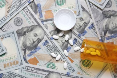 Bangkok, Thailand - January 07, 2022 : Pills and pill bottles scattered on US dollar bills.