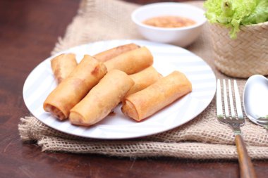 Kızarmış börek, sebze ve domatesle birlikte beyaz ahşap bir masada siyah bir tabağa konur ve sosu sosa batırır..