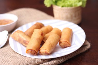 Kızarmış börek, sebze ve domatesle birlikte beyaz ahşap bir masada siyah bir tabağa konur ve sosu sosa batırır..