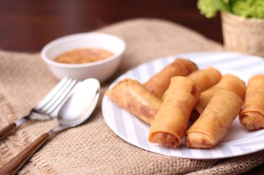 Kızarmış börek, sebze ve domatesle birlikte beyaz ahşap bir masada siyah bir tabağa konur ve sosu sosa batırır..