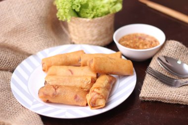 Kızarmış börek, sebze ve domatesle birlikte beyaz ahşap bir masada siyah bir tabağa konur ve sosu sosa batırır..