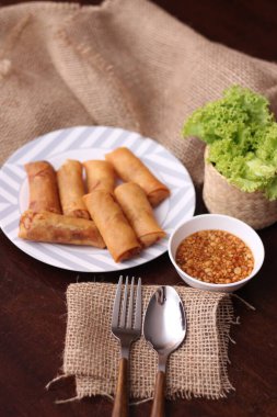 Kızarmış börek, sebze ve domatesle birlikte beyaz ahşap bir masada siyah bir tabağa konur ve sosu sosa batırır..