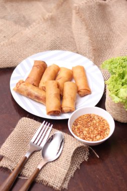 Kızarmış börek, sebze ve domatesle birlikte beyaz ahşap bir masada siyah bir tabağa konur ve sosu sosa batırır..