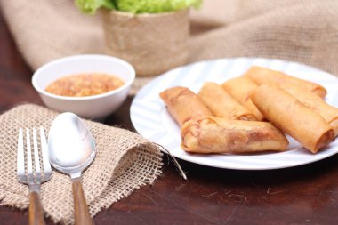 Kızarmış börek, sebze ve domatesle birlikte beyaz ahşap bir masada siyah bir tabağa konur ve sosu sosa batırır..
