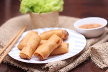 Kızarmış börek, sebze ve domatesle birlikte beyaz ahşap bir masada siyah bir tabağa konur ve sosu sosa batırır..