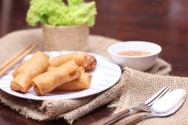 Kızarmış börek, sebze ve domatesle birlikte beyaz ahşap bir masada siyah bir tabağa konur ve sosu sosa batırır..