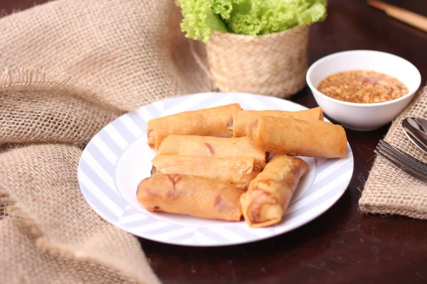 Fried spring rolls with vegetables and tomatoes placed in a black plate on a white wooden table and dipping sauce.