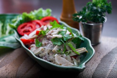 Baharatlı Vietnam sosisi salatası yaprak şeklindeki yeşil tabağa konur. Tayland 'da siyah ahşap bir masada soğan, sarımsak, kırmızı biber.