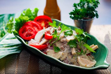 Baharatlı Vietnam sosisi salatası yaprak şeklindeki yeşil tabağa konur. Tayland 'da siyah ahşap bir masada soğan, sarımsak, kırmızı biber.