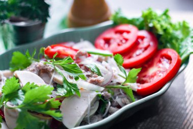 Baharatlı Vietnam sosisi salatası yaprak şeklindeki yeşil tabağa konur. Tayland 'da siyah ahşap bir masada soğan, sarımsak, kırmızı biber.