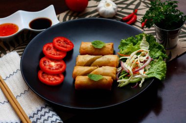 Kızarmış börek, sebzeler ve domateslerle siyah bir tabağa konmuş, ahşap bir masa ve tjhailand 'da sosa batırılmış..