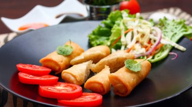 Kızarmış börek, sebzeler ve domateslerle siyah bir tabağa konmuş, ahşap bir masa ve tjhailand 'da sosa batırılmış..