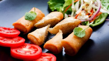 Kızarmış börek, sebzeler ve domateslerle siyah bir tabağa konmuş, ahşap bir masa ve tjhailand 'da sosa batırılmış..