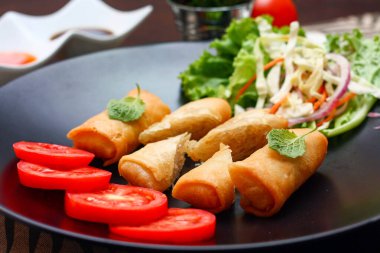 Kızarmış börek, sebzeler ve domateslerle siyah bir tabağa konmuş, ahşap bir masa ve tjhailand 'da sosa batırılmış..