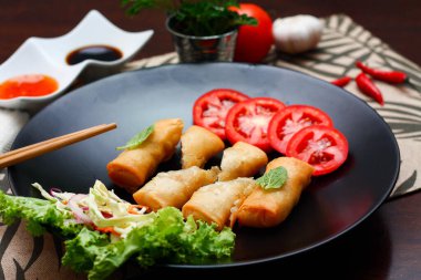 Kızarmış börek, sebzeler ve domateslerle siyah bir tabağa konmuş, ahşap bir masa ve tjhailand 'da sosa batırılmış..