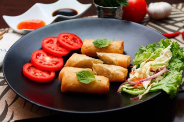 Kızarmış börek, sebzeler ve domateslerle siyah bir tabağa konmuş, ahşap bir masa ve tjhailand 'da sosa batırılmış..