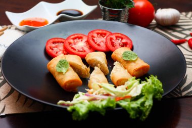 Kızarmış börek, sebzeler ve domateslerle siyah bir tabağa konmuş, ahşap bir masa ve tjhailand 'da sosa batırılmış..