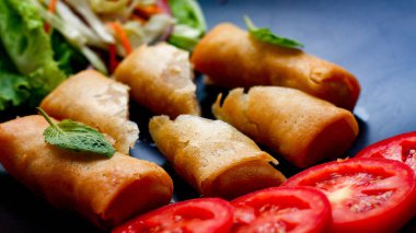 Kızarmış börek, sebzeler ve domateslerle siyah bir tabağa konmuş, ahşap bir masa ve tjhailand 'da sosa batırılmış..