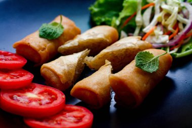 Kızarmış börek, sebzeler ve domateslerle siyah bir tabağa konmuş, ahşap bir masa ve tjhailand 'da sosa batırılmış..