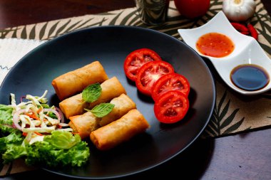 Kızarmış börek, sebzeler ve domateslerle siyah bir tabağa konmuş, ahşap bir masa ve tjhailand 'da sosa batırılmış..