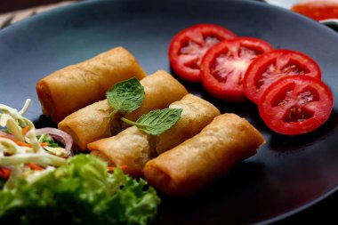 Kızarmış börek, sebzeler ve domateslerle siyah bir tabağa konmuş, ahşap bir masa ve tjhailand 'da sosa batırılmış..