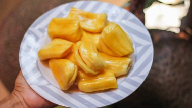 Jackfruit beyaz bir tabakta taze, Tayland 'da kaya meyvesi dallarıyla ahşap bir masaya yerleştirilmiş..