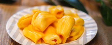 Jackfruit beyaz bir tabakta taze, Tayland 'da kaya meyvesi dallarıyla ahşap bir masaya yerleştirilmiş..