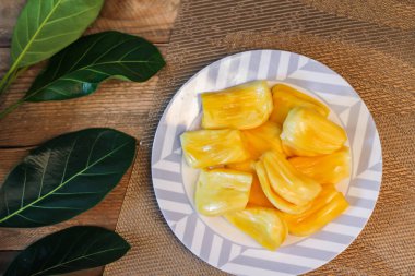 Jackfruit beyaz bir tabakta taze, Tayland 'da kaya meyvesi dallarıyla ahşap bir masaya yerleştirilmiş..