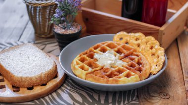 Gri bir tabakta balla kaplanmış waffleların üzerinde ekmek ve baharatlar restorandaki ahşap bir masaya konmuş..