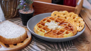 Gri bir tabakta balla kaplanmış waffleların üzerinde ekmek ve baharatlar restorandaki ahşap bir masaya konmuş..