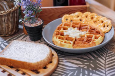 Gri bir tabakta balla kaplanmış waffleların üzerinde ekmek ve baharatlar restorandaki ahşap bir masaya konmuş..