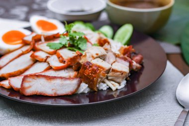 Buharda pilav ve kırmızı domuz eti, siyah tabakta çıtır domuz eti sosu ve soya sosuyla servis edilir siyah ahşap bir masanın üzerine yerleştirilir. Asya 'da yemek.