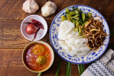 Fıstık soslu Tayland pilavı, ahşap bir masada servis edilir ve yapraklarla süslenir..