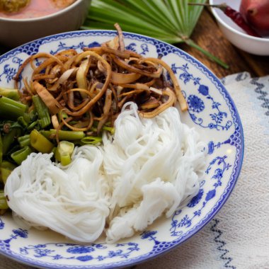 Fıstık soslu Tayland pilavı, ahşap bir masada servis edilir ve yapraklarla süslenir..
