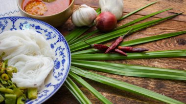 Fıstık soslu Tayland pilavı, ahşap bir masada servis edilir ve yapraklarla süslenir..