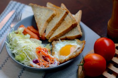Kahvaltı, sahanda yumurta, kızarmış sosis, sebze salatası ve kahverengi ahşap bir masada tost ve Tayland kahvesi..